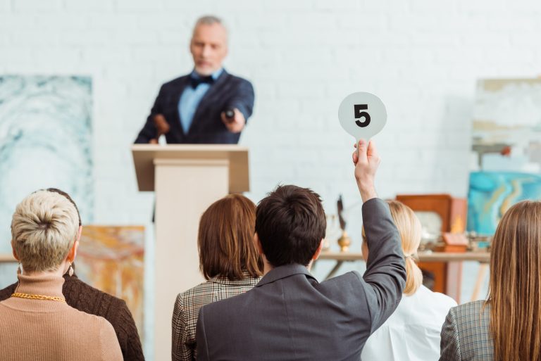 An auctioneer takes bids from a rostrum as a bidder raises a paddle