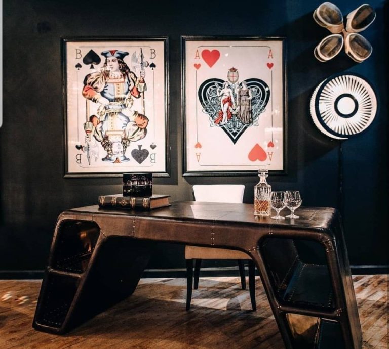 Sculptural dark wood desk beneath framed playing-card artwork in a panelled study