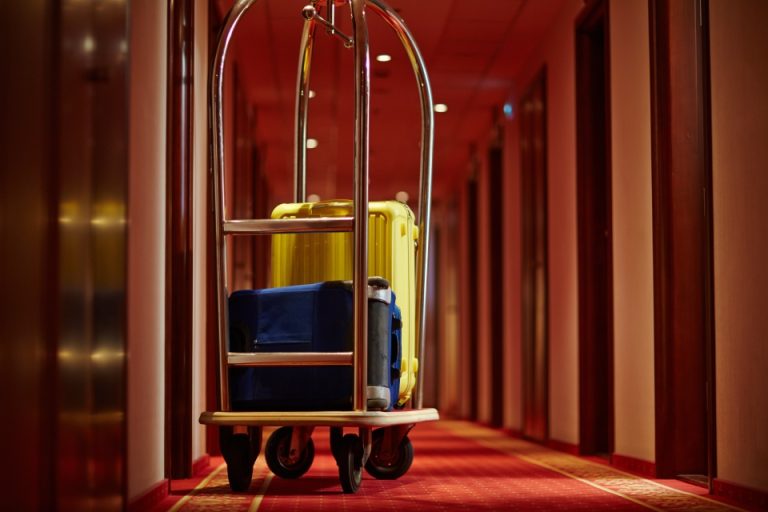 Brass hotel luggage trolley loaded with cases in a red-lit corridor